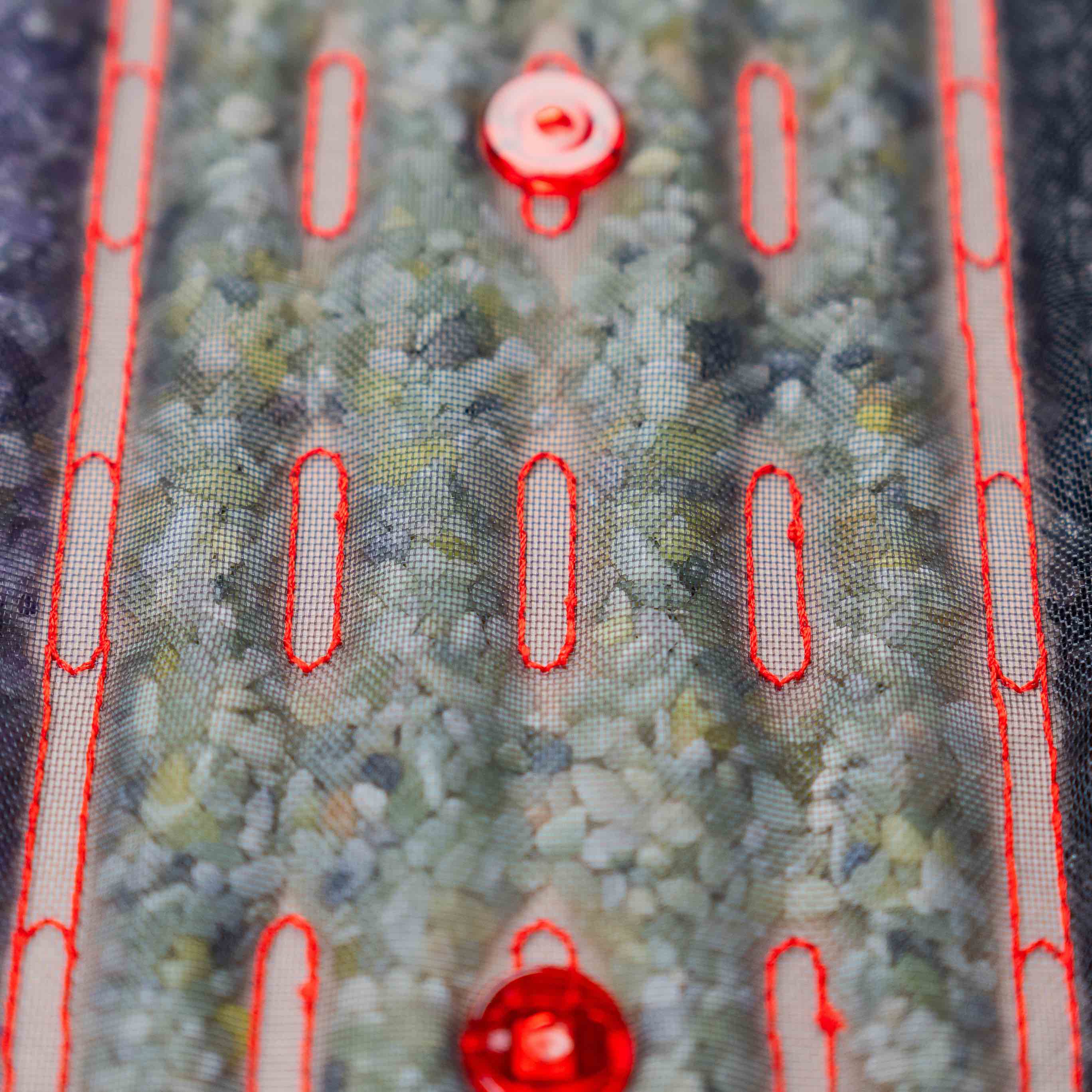 Zbliżenie na kamienie masujące pod siatkową powierzchnią podgrzewanej maty Casada, z widocznymi czerwonymi diodami LED i przeszyciami.