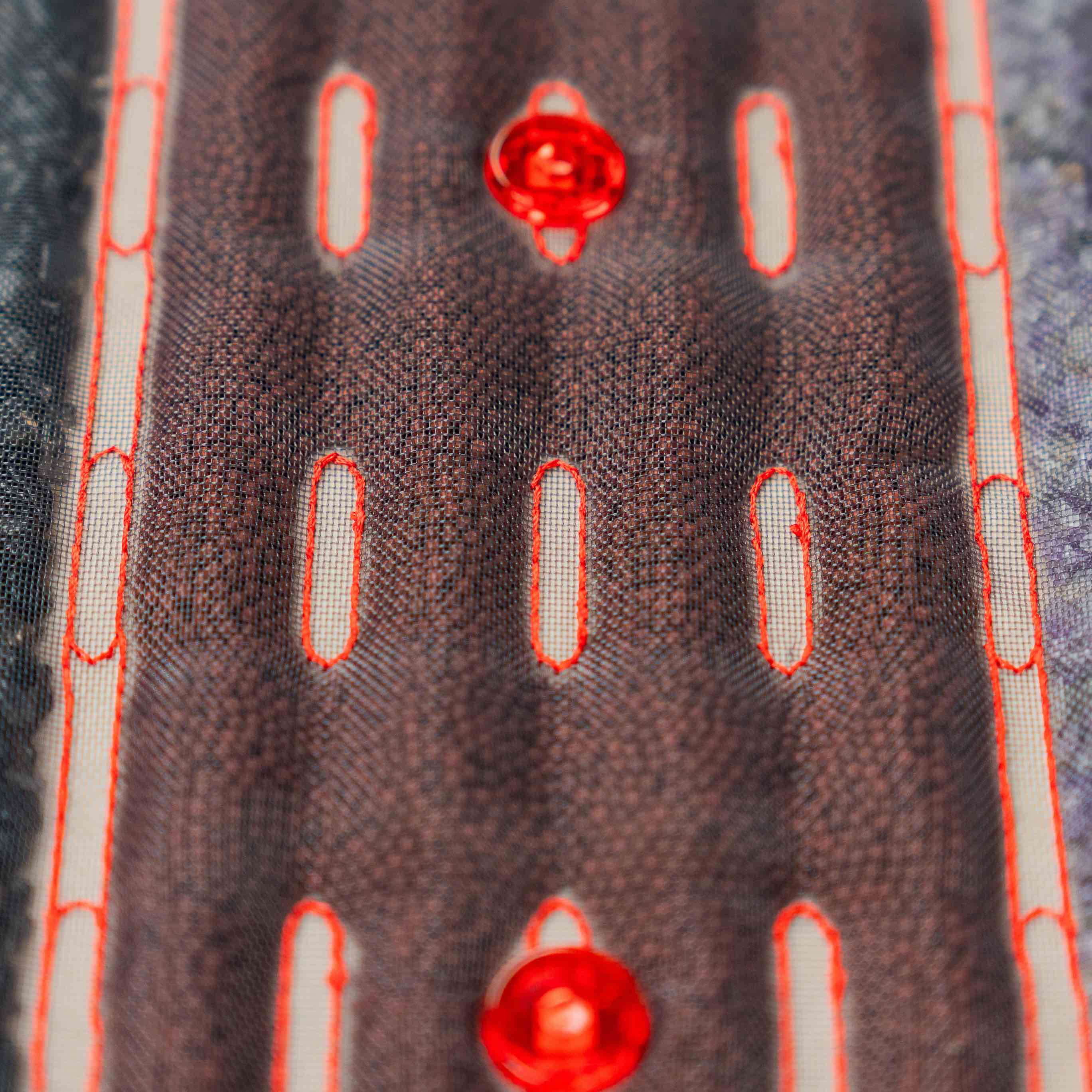 Zbliżenie na kamienie masujące pod siatkową powierzchnią podgrzewanej maty Casada, z widocznymi czerwonymi diodami LED i przeszyciami.