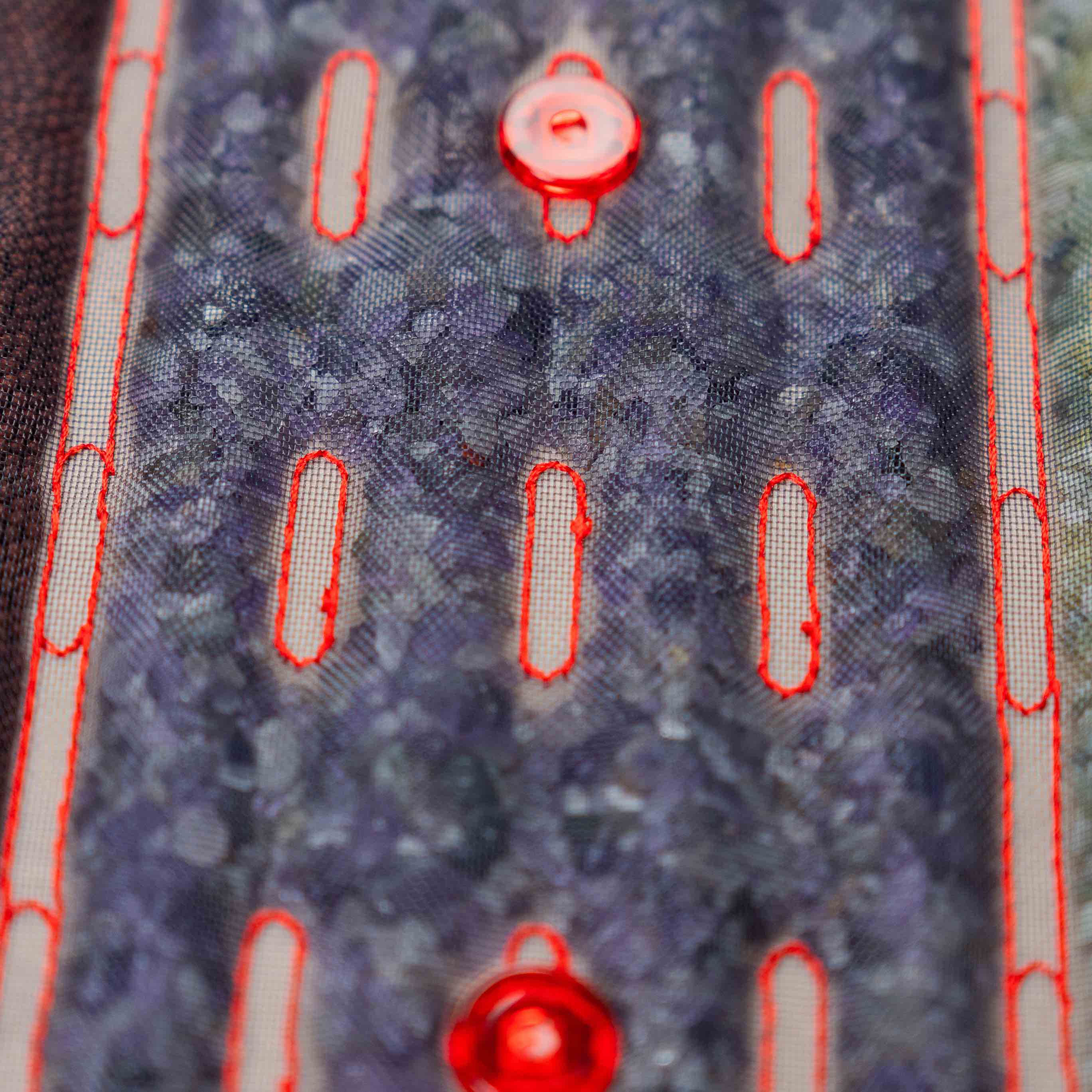 Zbliżenie na kamienie masujące pod siatkową powierzchnią podgrzewanej maty Casada, z widocznymi czerwonymi diodami LED i przeszyciami.