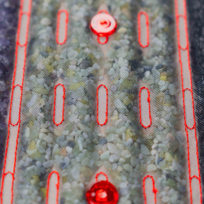 Zbliżenie na kamienie masujące pod siatkową powierzchnią podgrzewanej maty Casada, z widocznymi czerwonymi diodami LED i przeszyciami.