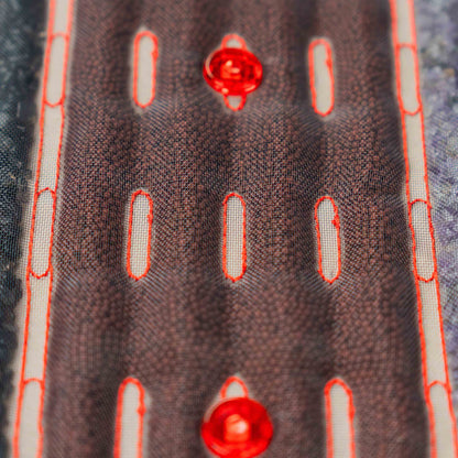 Zbliżenie na kamienie masujące pod siatkową powierzchnią podgrzewanej maty Casada, z widocznymi czerwonymi diodami LED i przeszyciami.