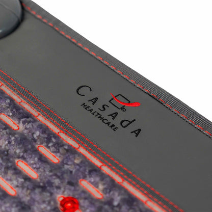 Zbliżenie na logo Casada Healthcare na krawędzi podgrzewanej maty masującej, z widocznymi czerwonymi przeszyciami i elementami LED.