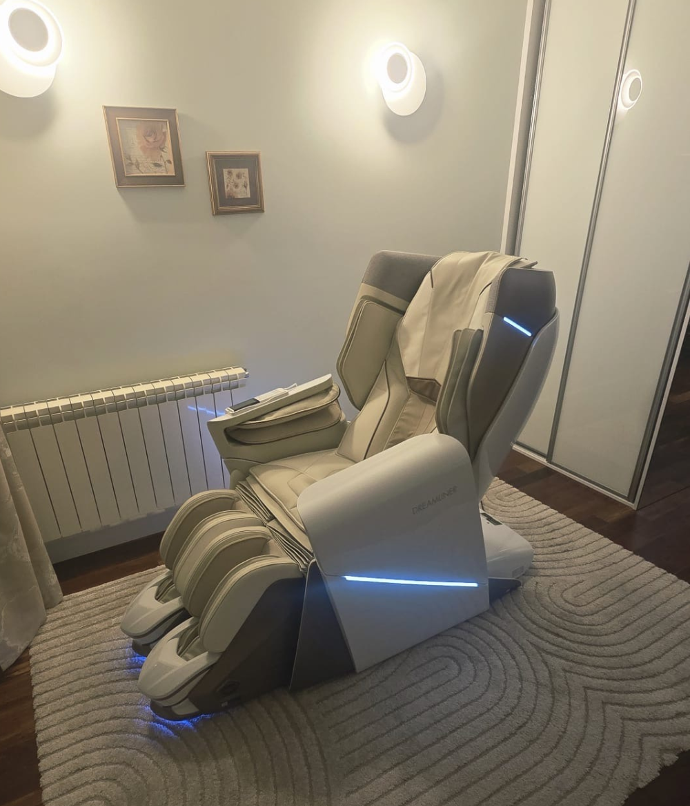 Kremowy fotel masujący Dreamliner, stojący w przytulnym pokoju na kremowym, puszystym dywaniku. 