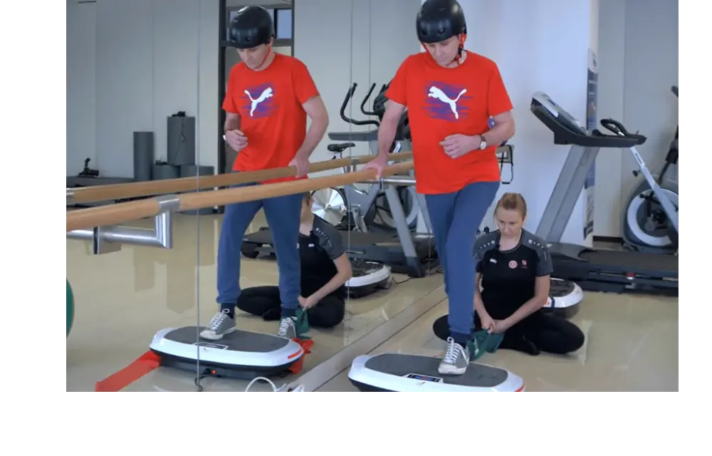 Mężczyzna w kasku poddawany jest rehabilitacji na platformie wibracyjnej PowerBoard.